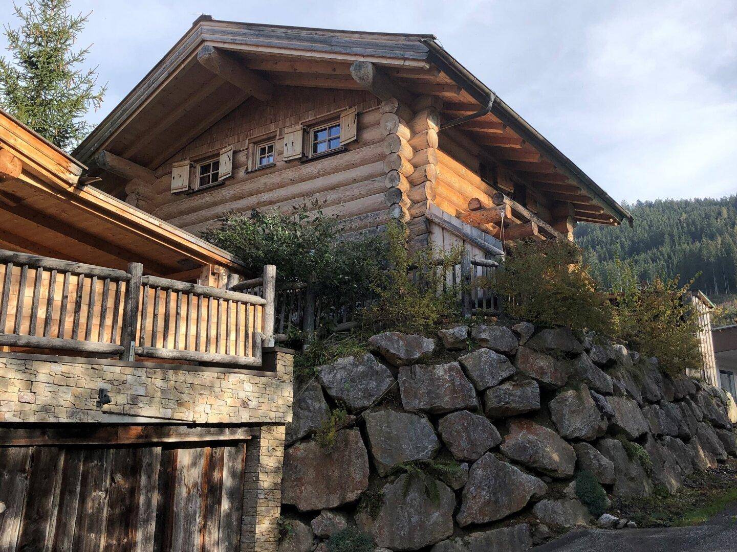 Holzhaus auf einem Hanggrundstück mit großer Steinmauer und Balkon.