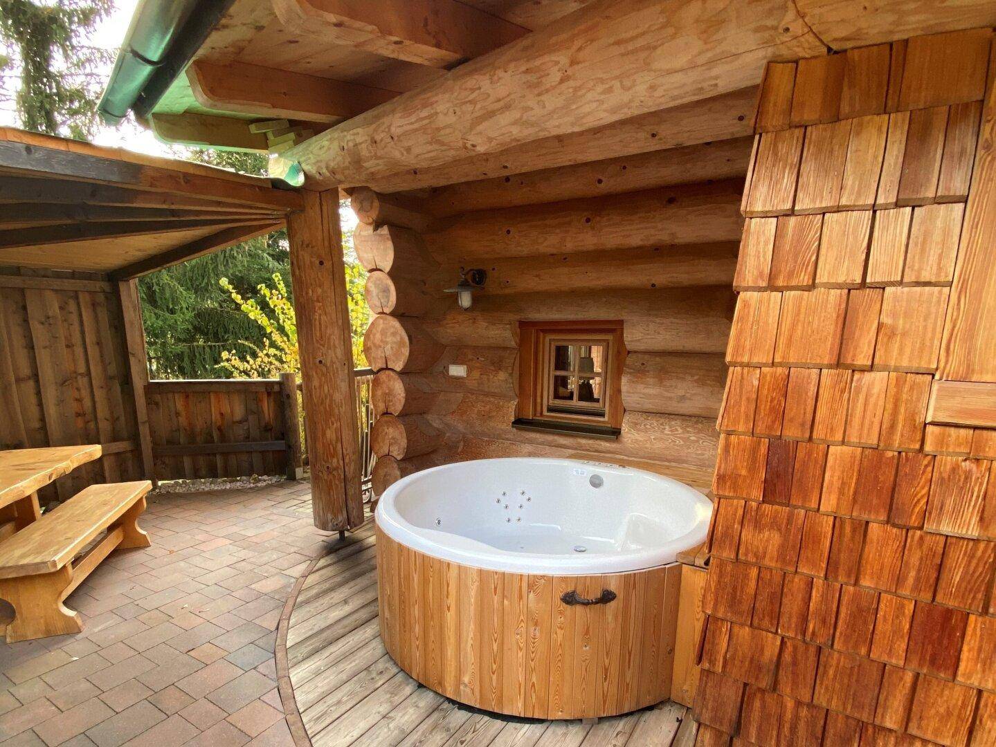 Überdachte Terrasse mit Whirlpool und Holztisch, umgeben von Holzverkleidung.