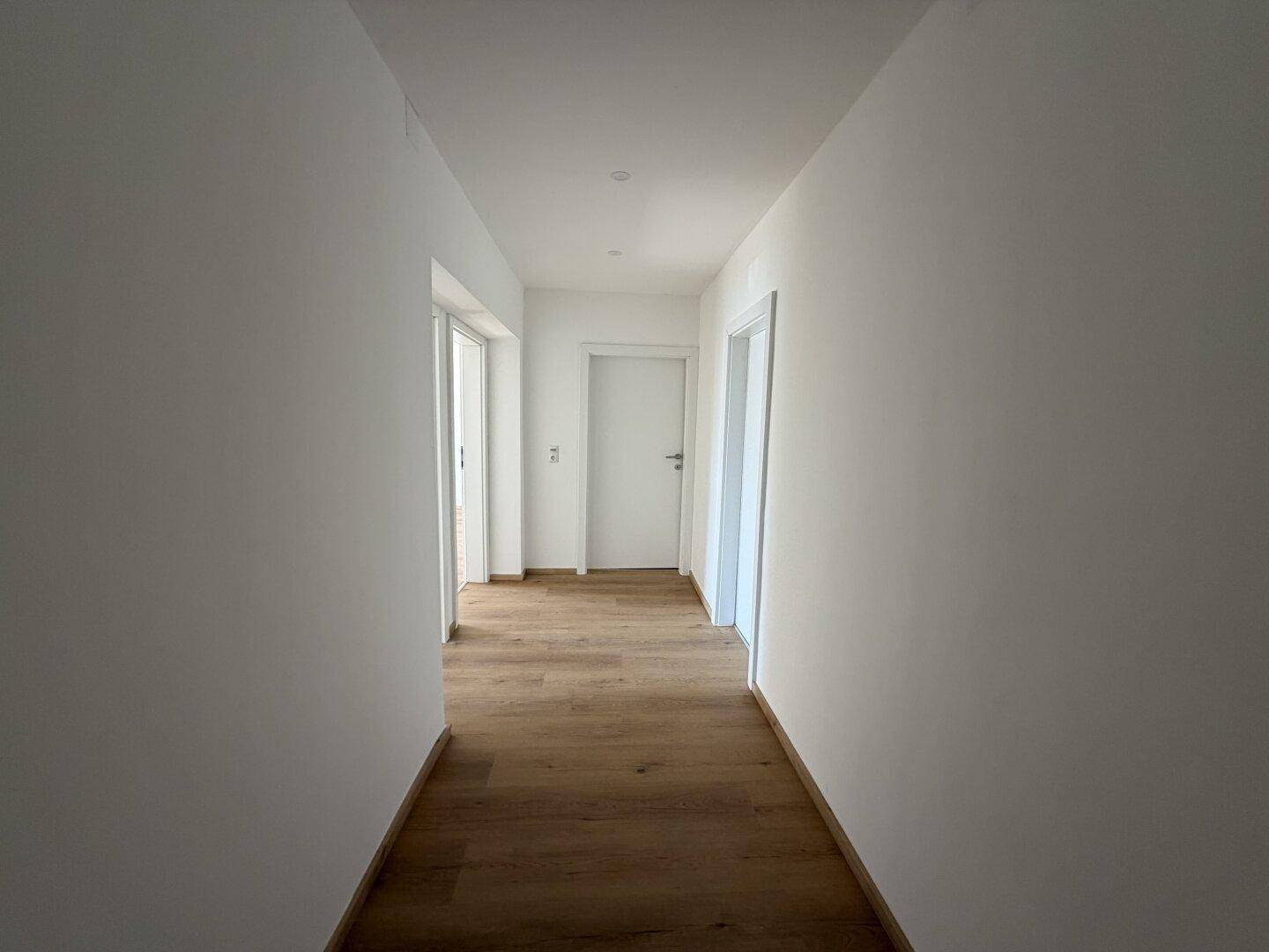 Heller Flur mit Holzboden und weißen Wänden, der zu verschiedenen Räumen führt.