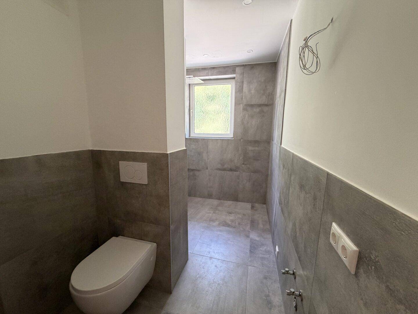Modernes Badezimmer mit wandhängender Toilette und grauen Fliesen, im Bau befindlich.