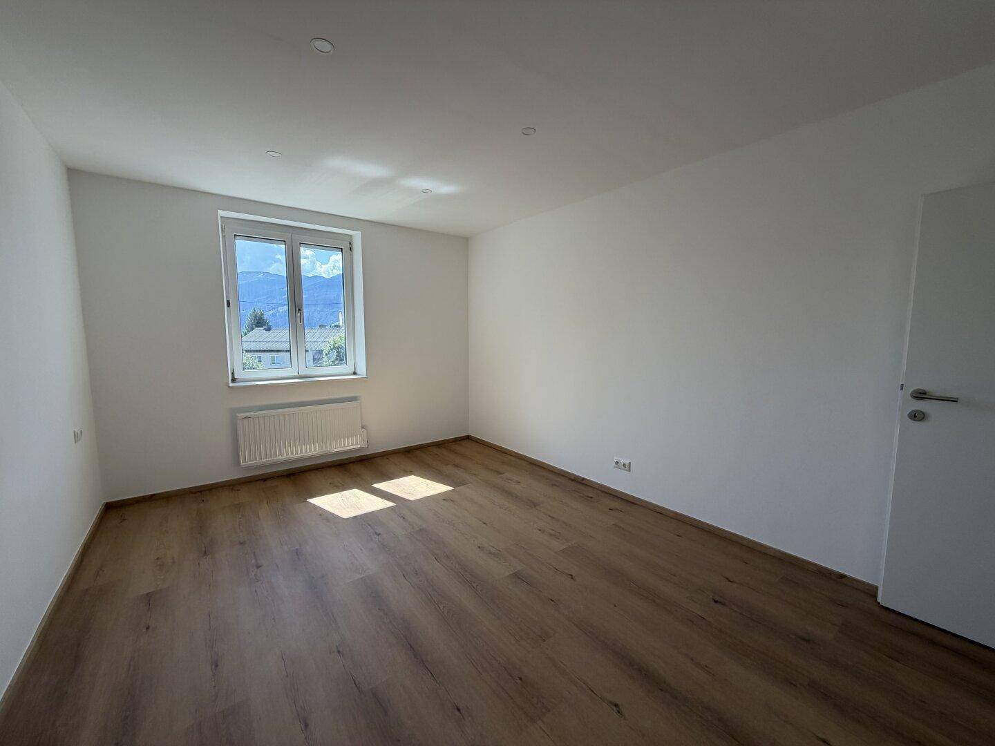 Helles, leeres Zimmer mit Holzboden und Bergblick durch das Fenster.