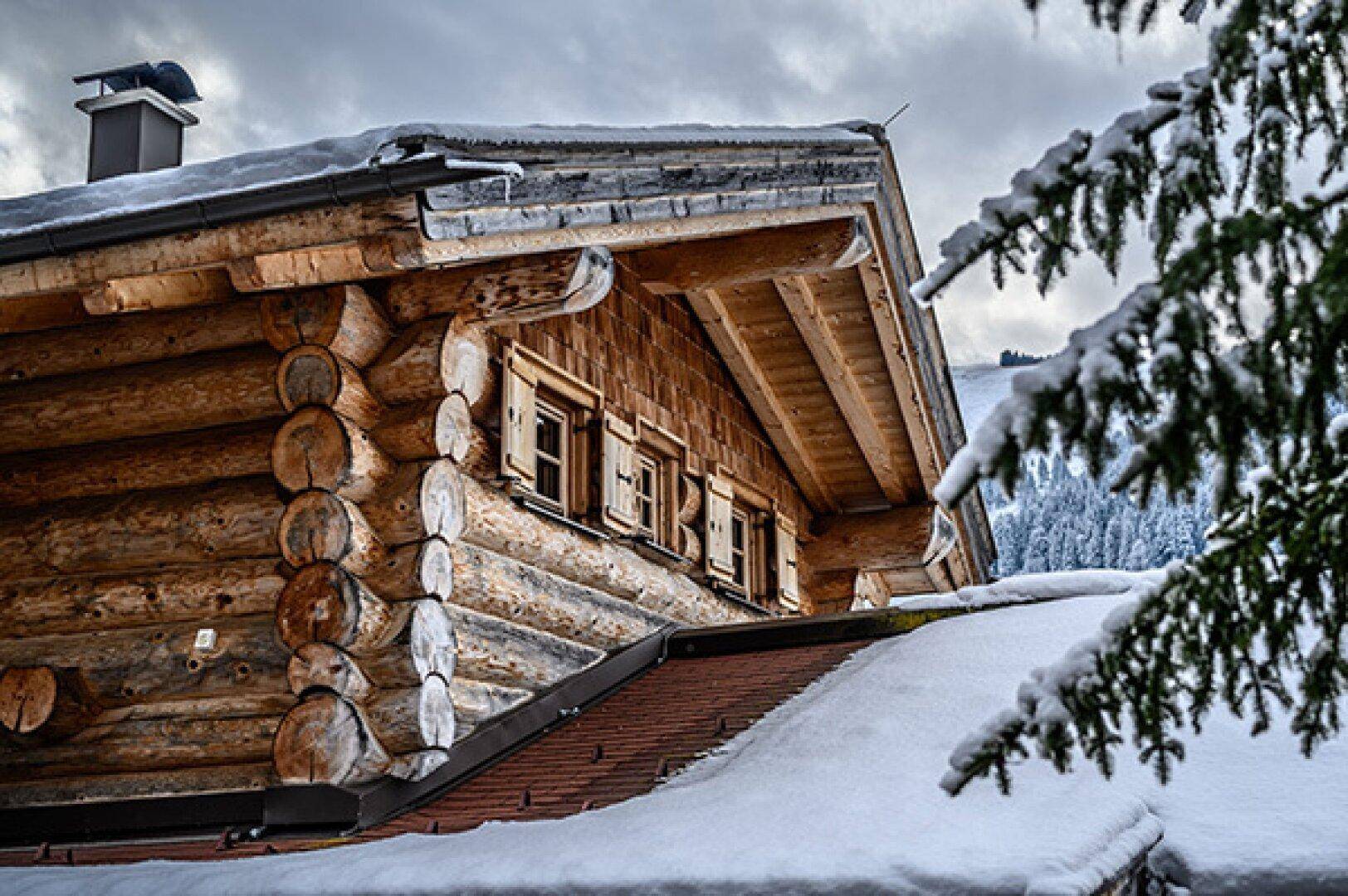Detailansicht eines Holzhauses mit verschneitem Dach, traditionellen Fensterläden und Holzbalken.