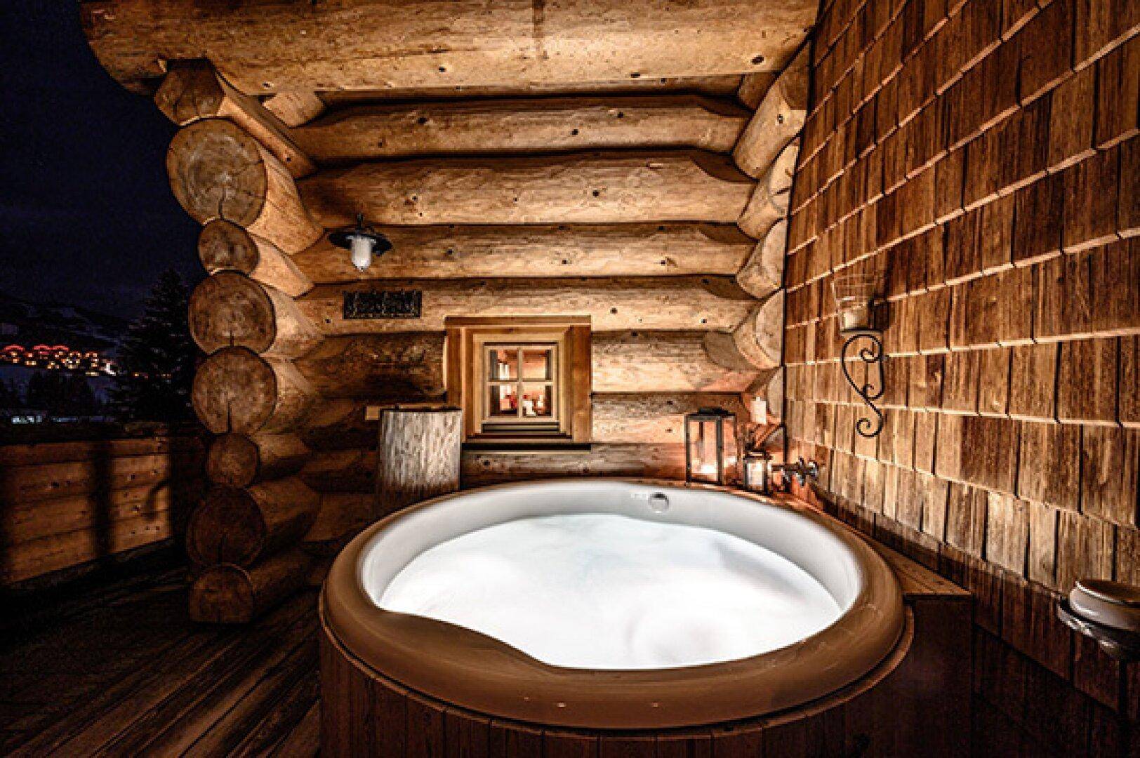 Außenwhirlpool auf einer Holzterrasse bei Nacht, umgeben von rustikalen Holzwänden und Laternen.