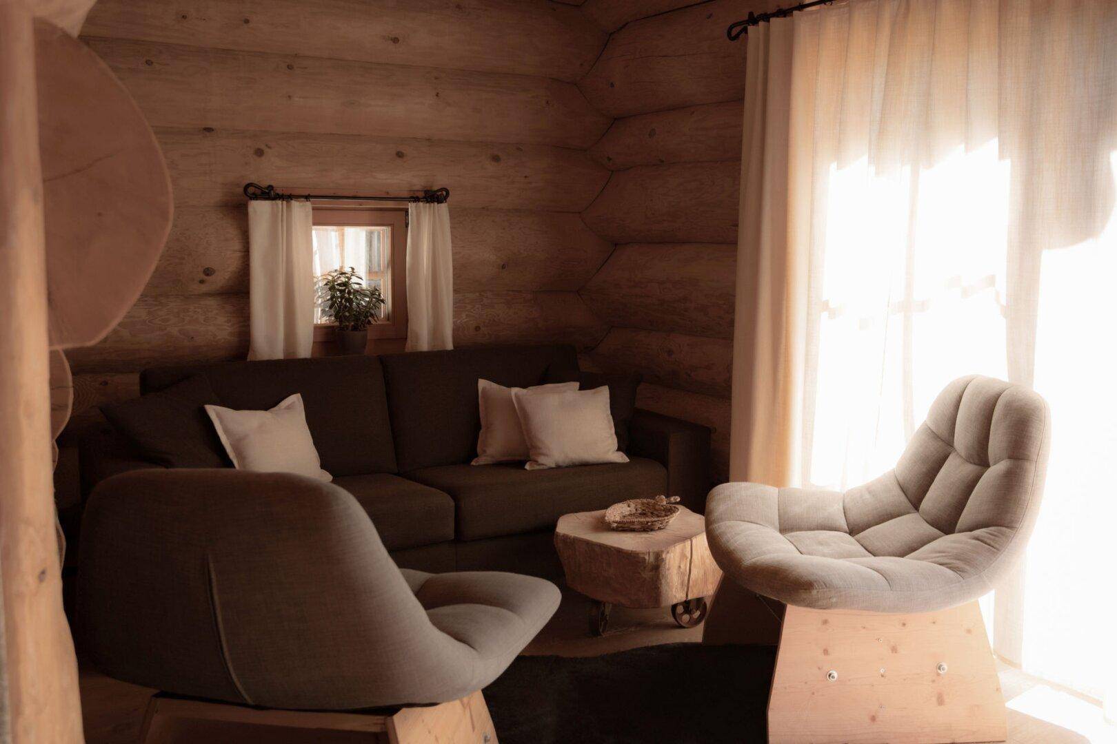 Heller Wohnbereich in einem Holzhaus mit bequemen Sesseln, Sofa und einem kleinen Fenster.