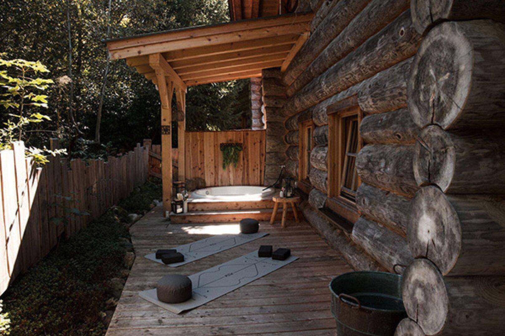 Holzterrasse mit Whirlpool und Yogamatten, umgeben von Bäumen und einem Holzzaun.