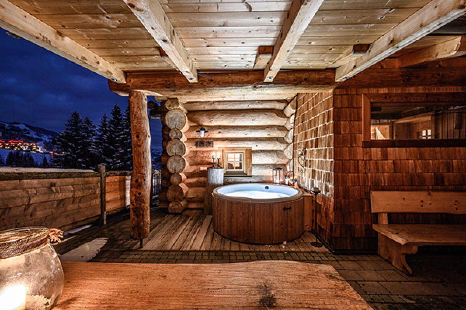 Überdachte Holzterrasse mit Whirlpool und Sitzbank bei Dämmerung, mit Bergblick.