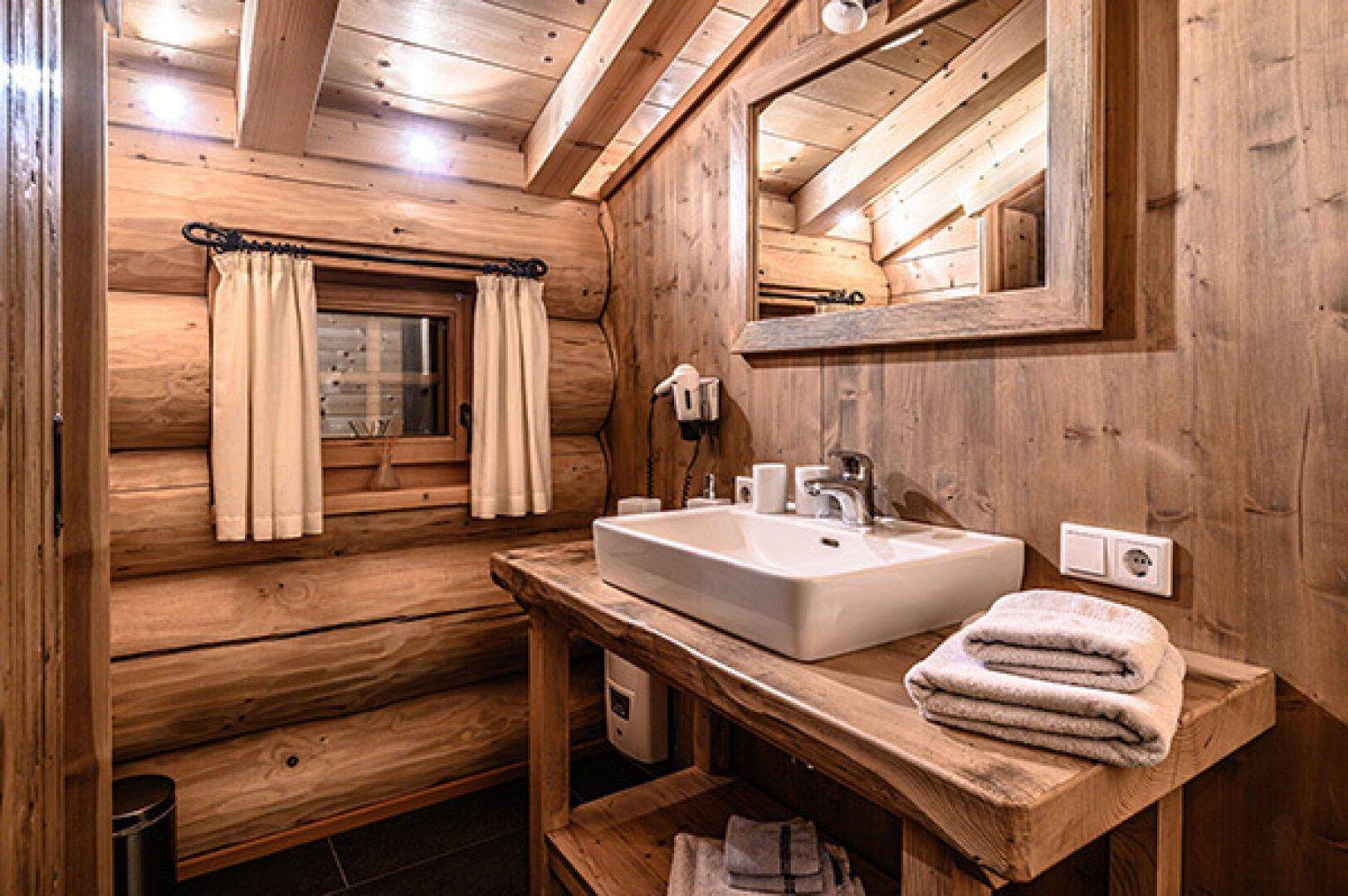 Badezimmer in einem Holzhaus mit Waschbecken auf Holzplatte und Fenster.