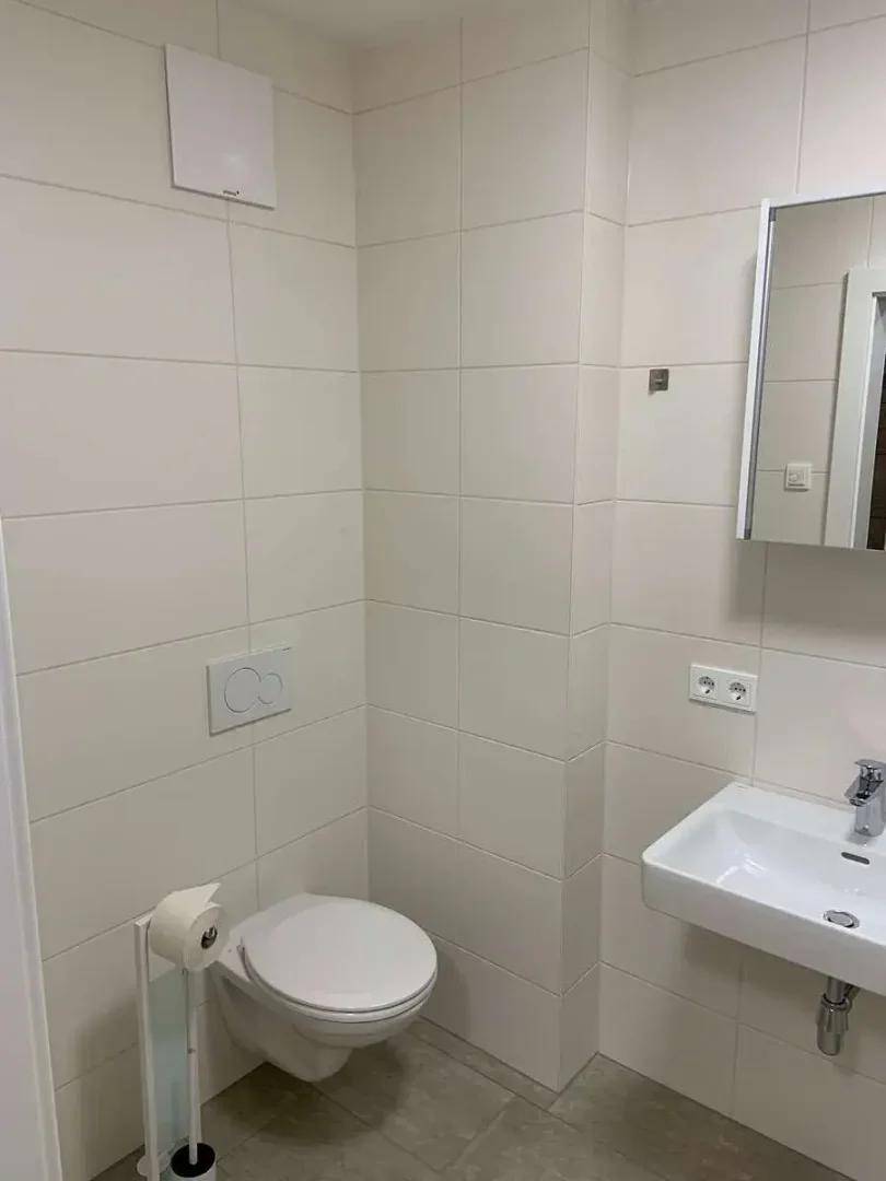 Funktionales Badezimmer mit wandhängendem WC, Waschbecken und hellen Fliesen.