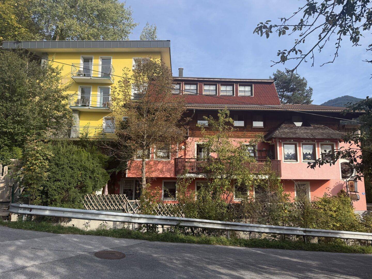 Nahaufnahme von zwei Gebäuden, eines gelb mit Balkonen, das andere rosa mit traditionellen Holzdetails und Dachgauben.