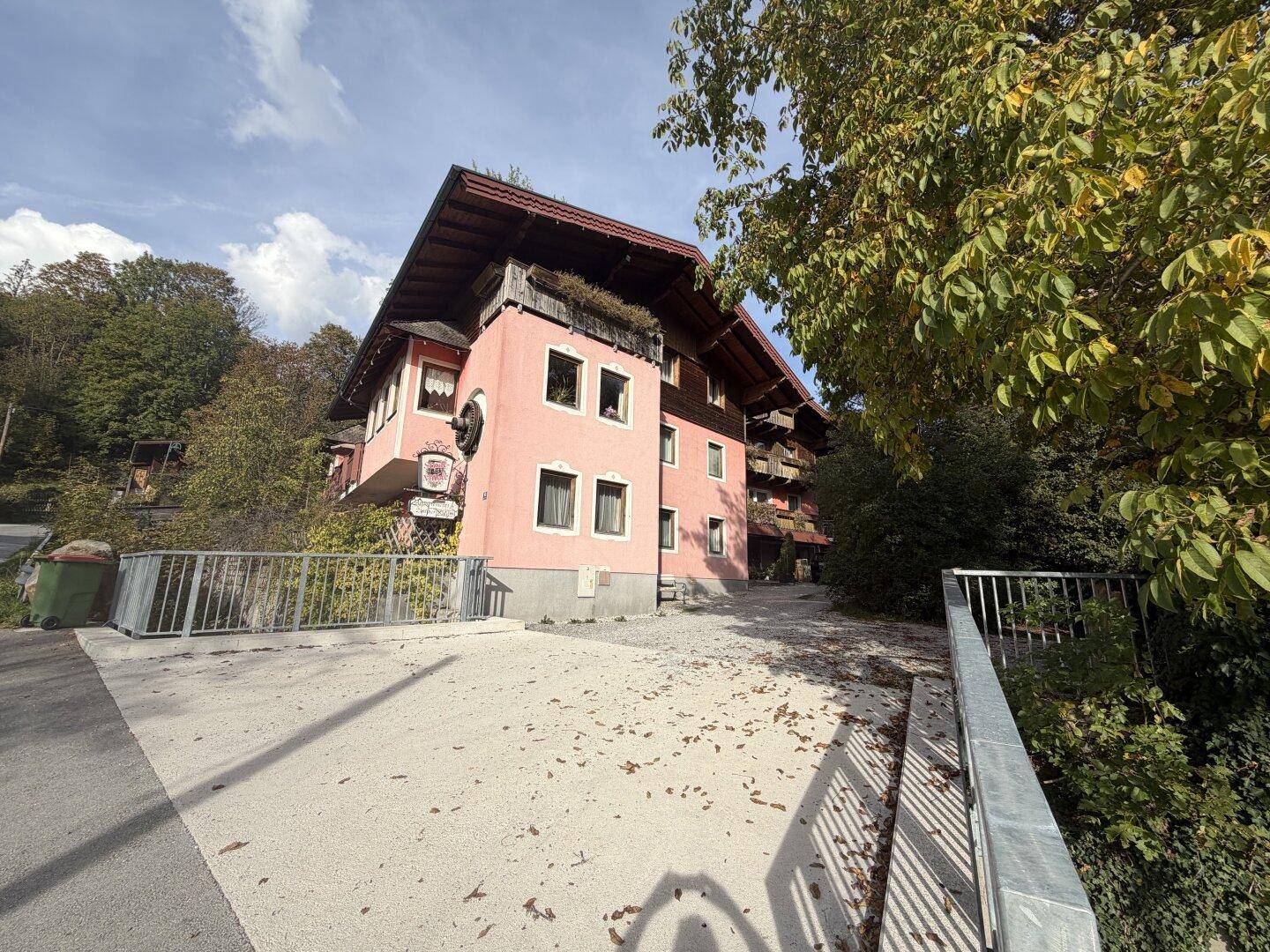 Traditionelles rosa Gebäude mit Holzbalkonen und einem breiten Dachüberstand in einer ländlichen Umgebung.