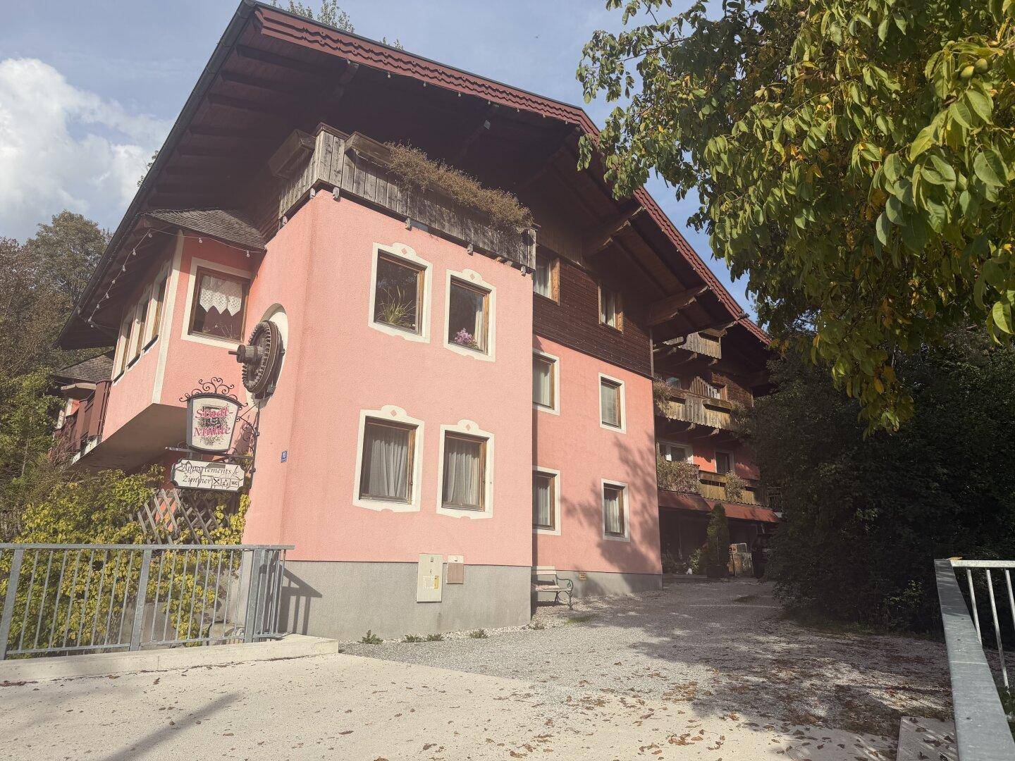 Rosa gestrichenes Gebäude mit traditionellen Holzdetails, einem großen, überhängenden Dach und einem Eingangsbereich.