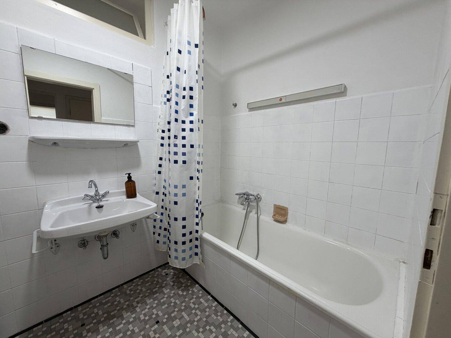 Badezimmer mit Badewanne, Duschvorhang, Waschbecken und einem Spiegelschrank über dem Waschplatz.