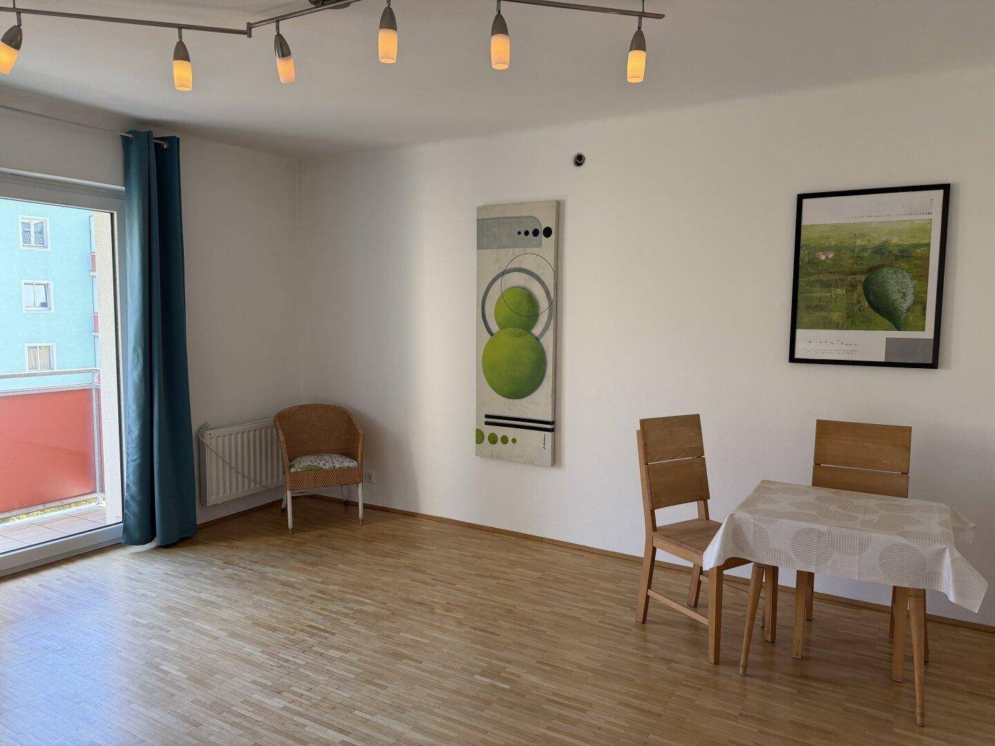 Heller Wohn- und Essbereich mit Parkettboden, Esstisch und Zugang zu einem Balkon durch eine große Fenstertür.