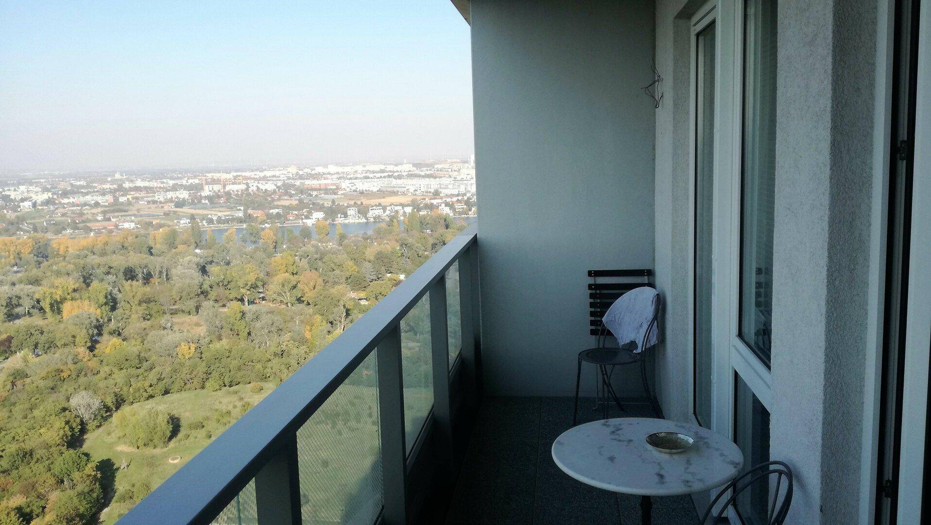 Kleiner Balkon mit Tisch und Stuhl, bietet einen weiten Blick über die Stadt und grüne Umgebung.