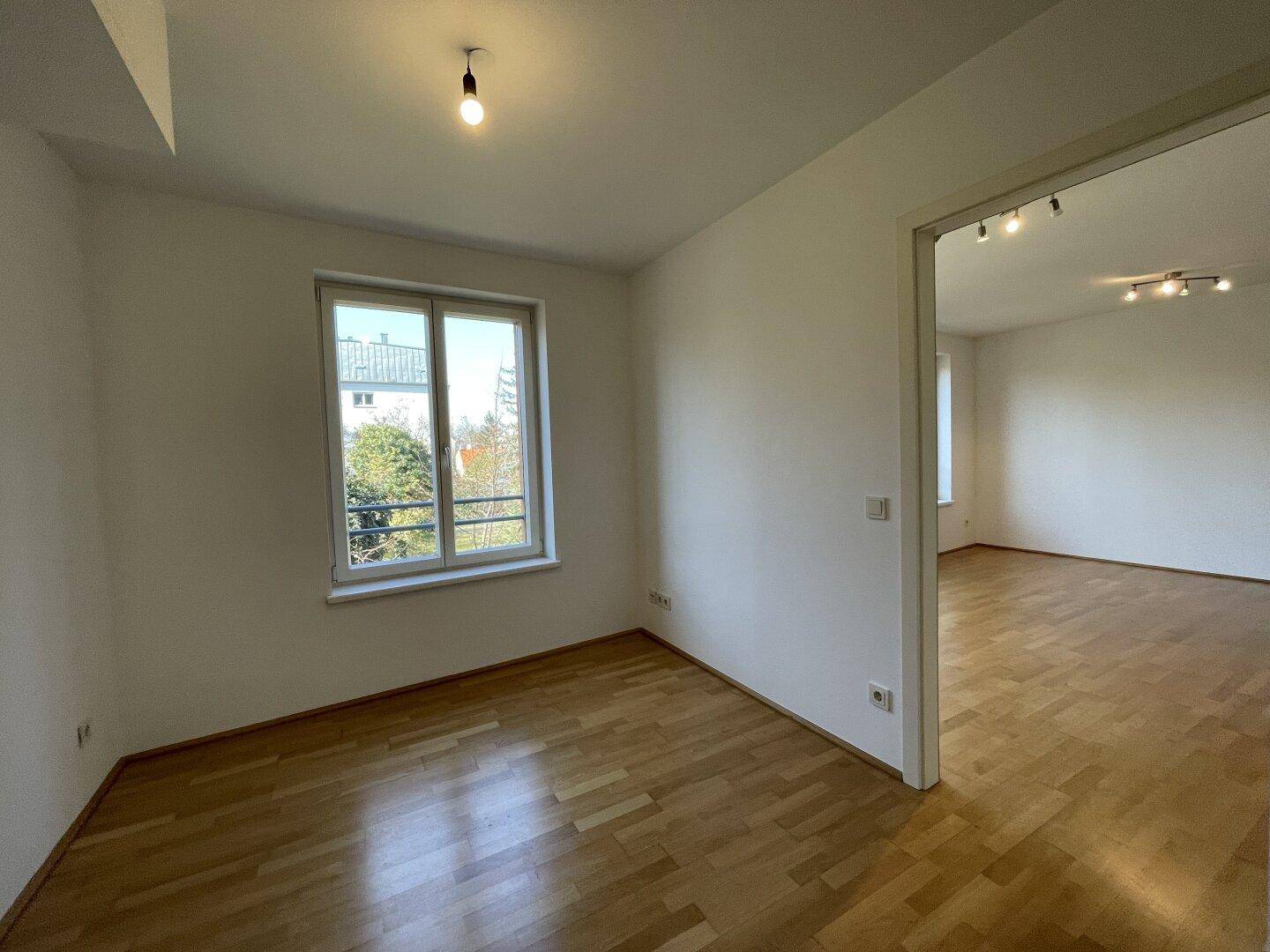 Ruhiges Zimmer mit Parkettboden und Fenster, das einen Blick ins Grüne ermöglicht.