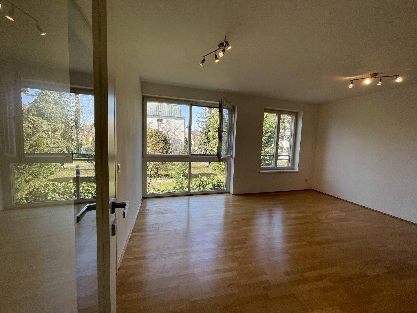 Geräumiges Wohnzimmer mit hellem Parkettboden und Blick auf die umliegende Grünfläche.