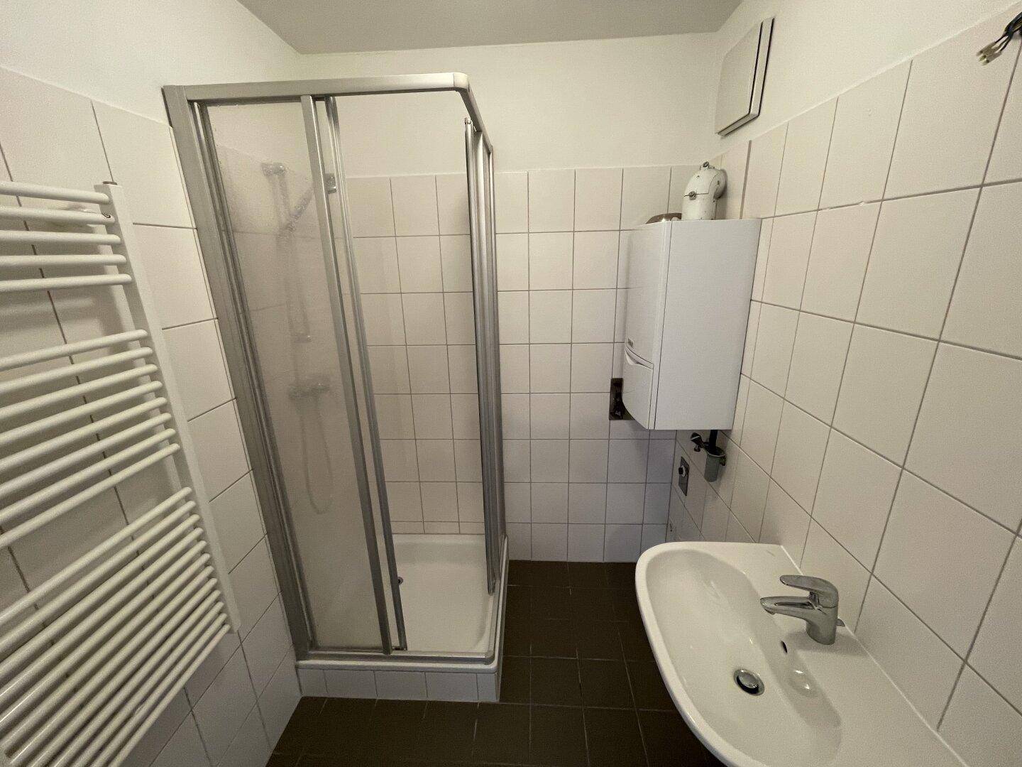 Gefliestes Badezimmer mit Duschkabine, Waschbecken und beheiztem Handtuchhalter.