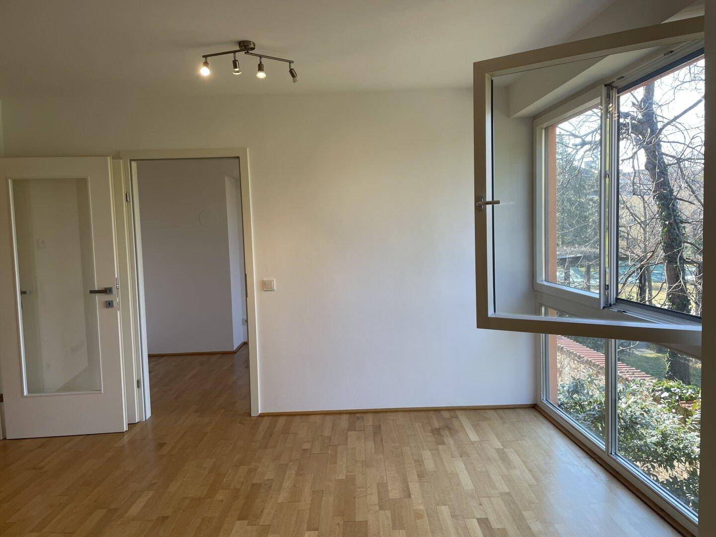 Lichtdurchfluteter Wohnraum mit Parkettboden und großen Fenstern, die einen weiten Blick bieten.