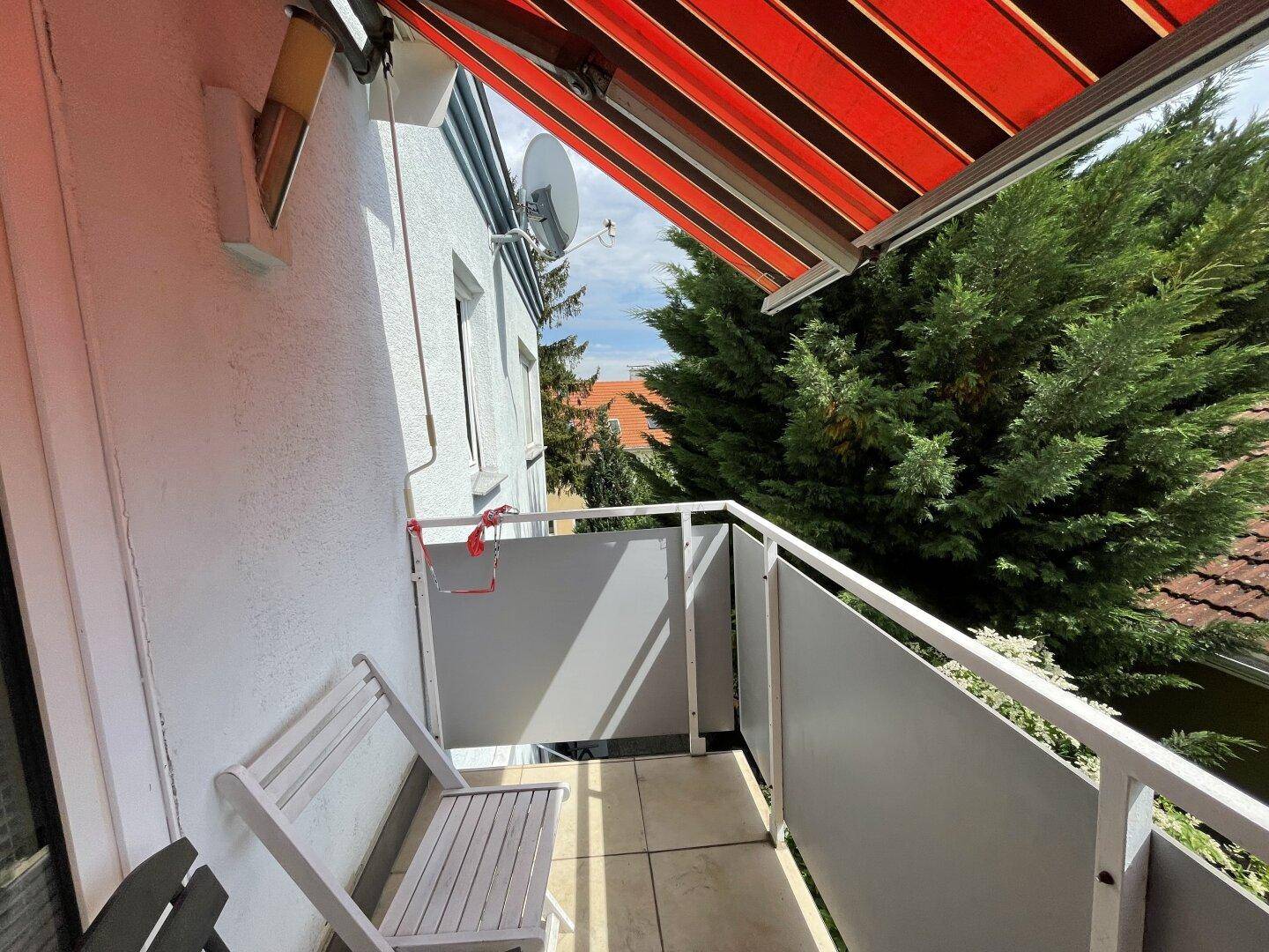 Kleiner Balkon mit Markise und Sitzgelegenheit, umgeben von Bäumen und mit Blick ins Grüne.