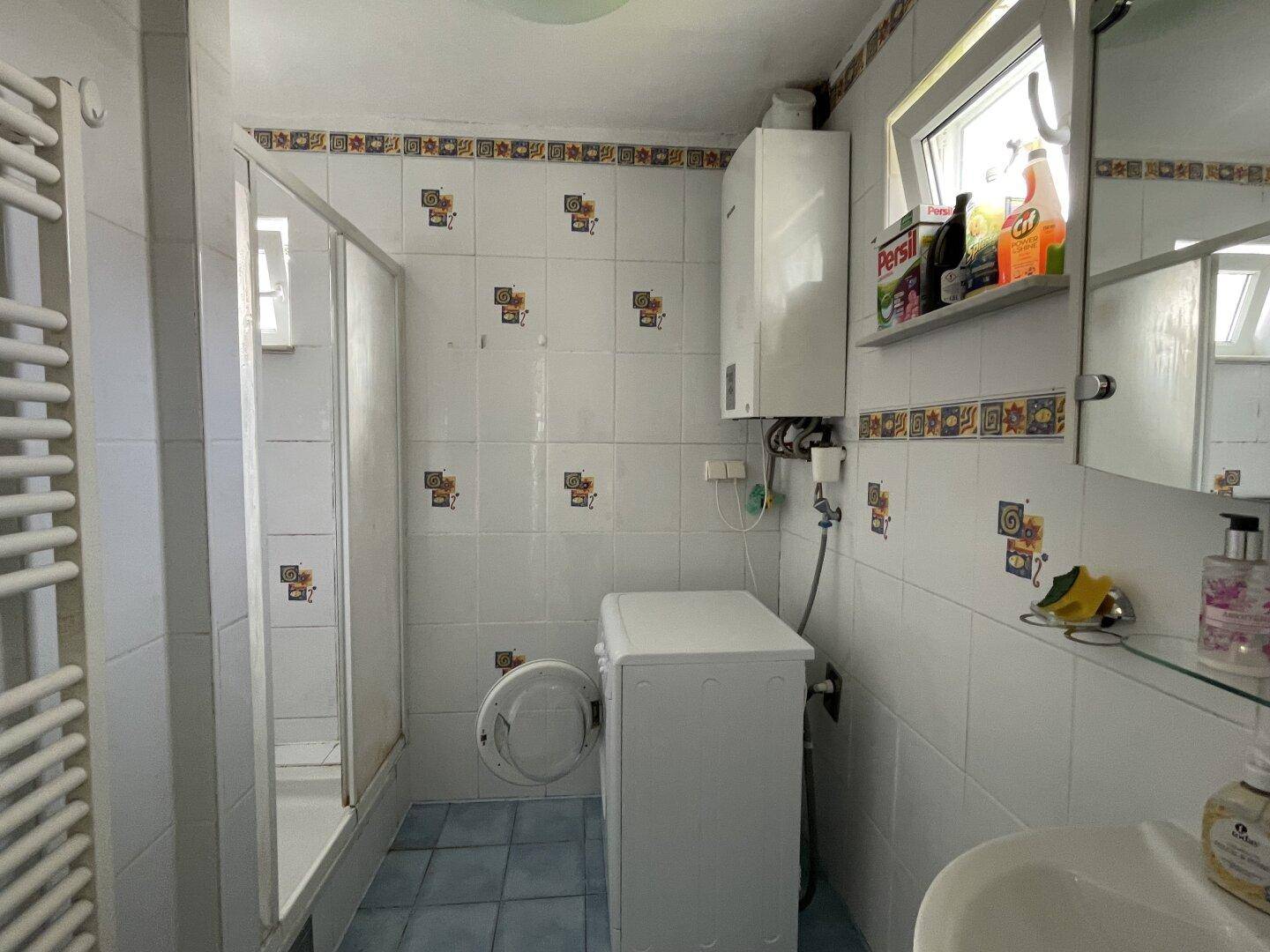 Gefliestes Badezimmer mit Dusche, Waschmaschine und Fenster, in gutem Zustand.