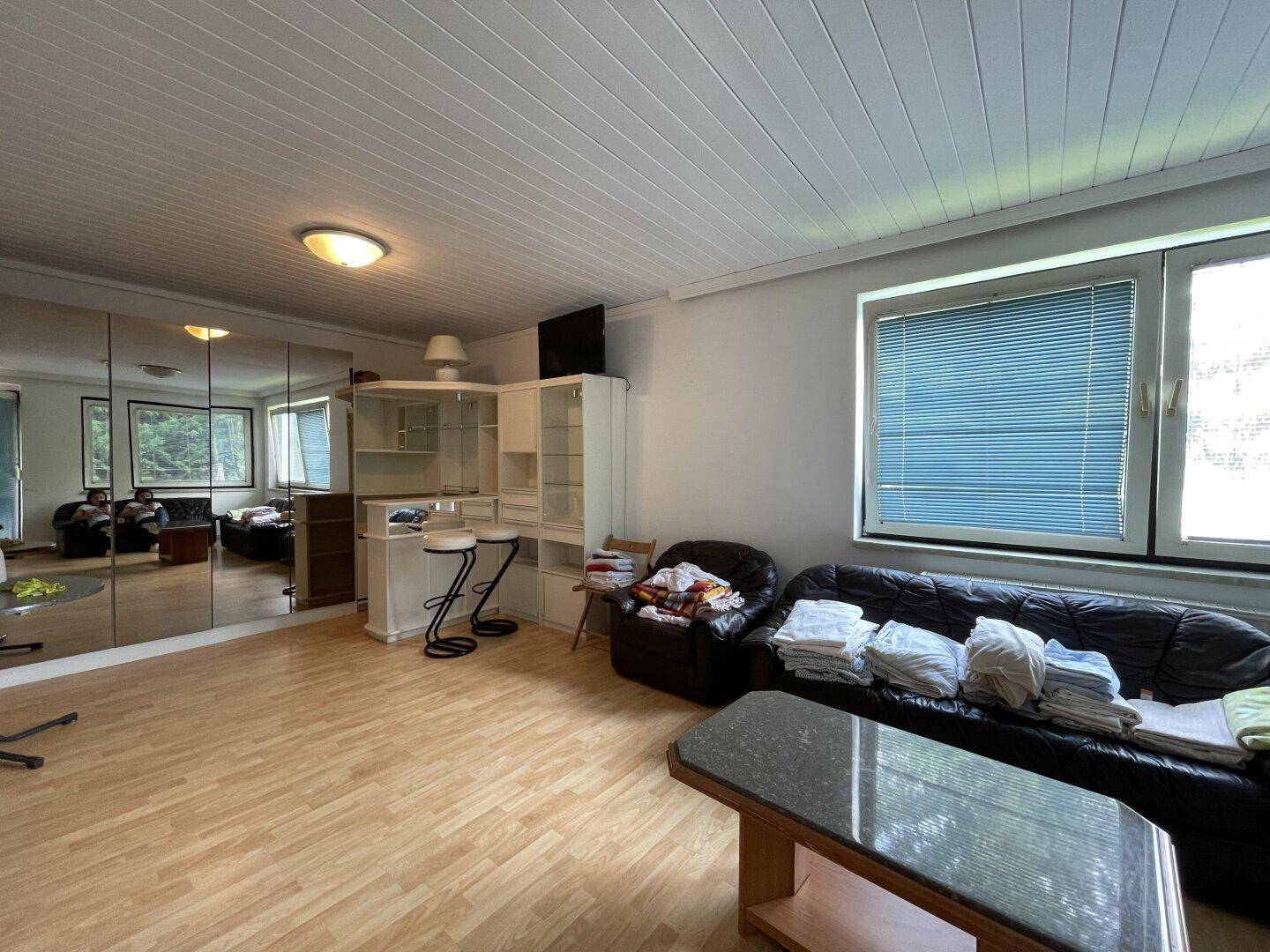 Geräumiges Wohnzimmer mit Holzboden, Spiegelfront und Sitzbereich mit Bar.