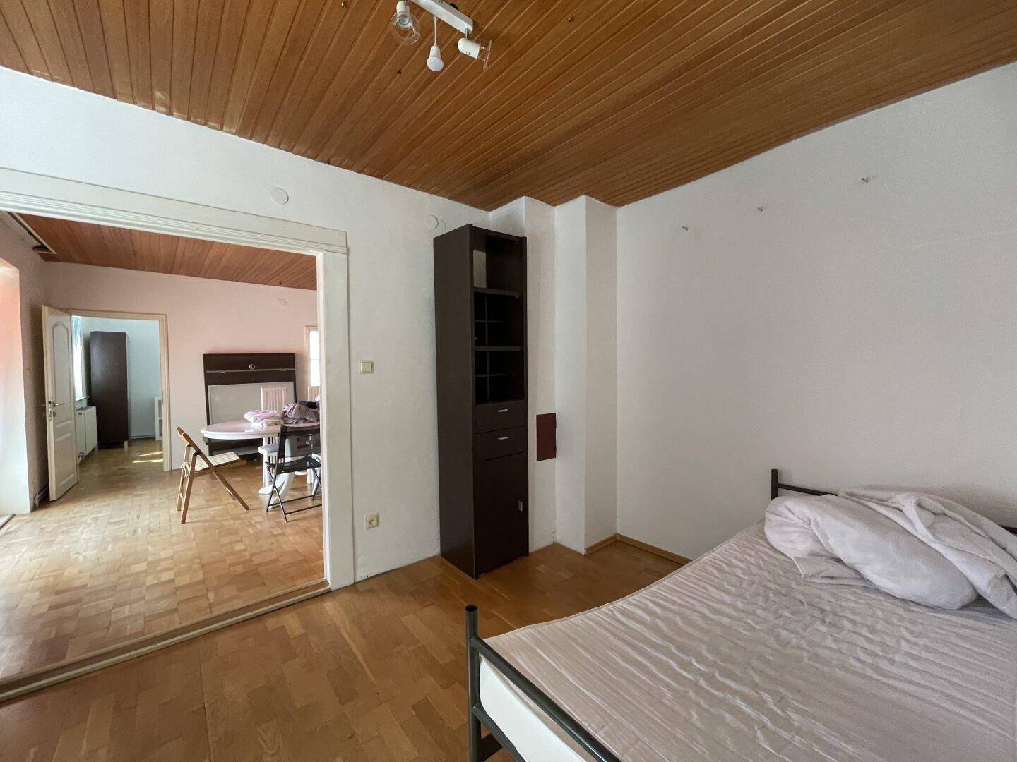 Schlafzimmer mit Holzboden und Holzdecke, offen zu einem angrenzenden Essbereich.
