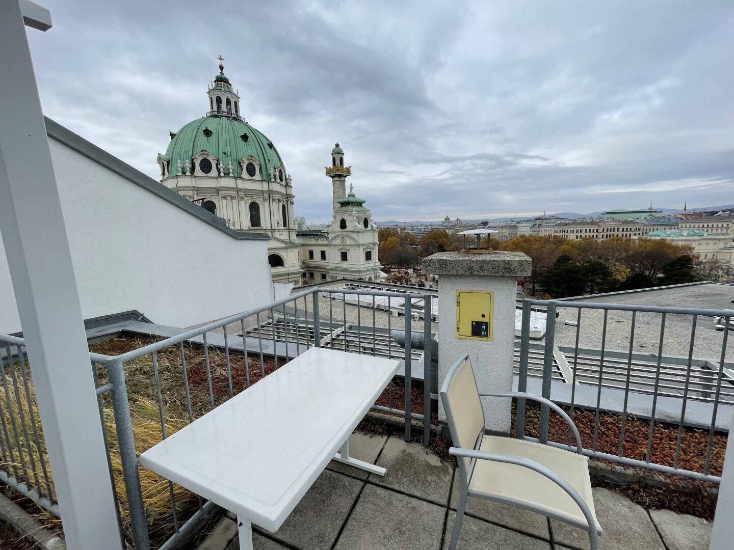 Dachterrasse mit Sitzgelegenheiten und beeindruckendem Blick auf die Karlskirche, ideal zum Entspannen.