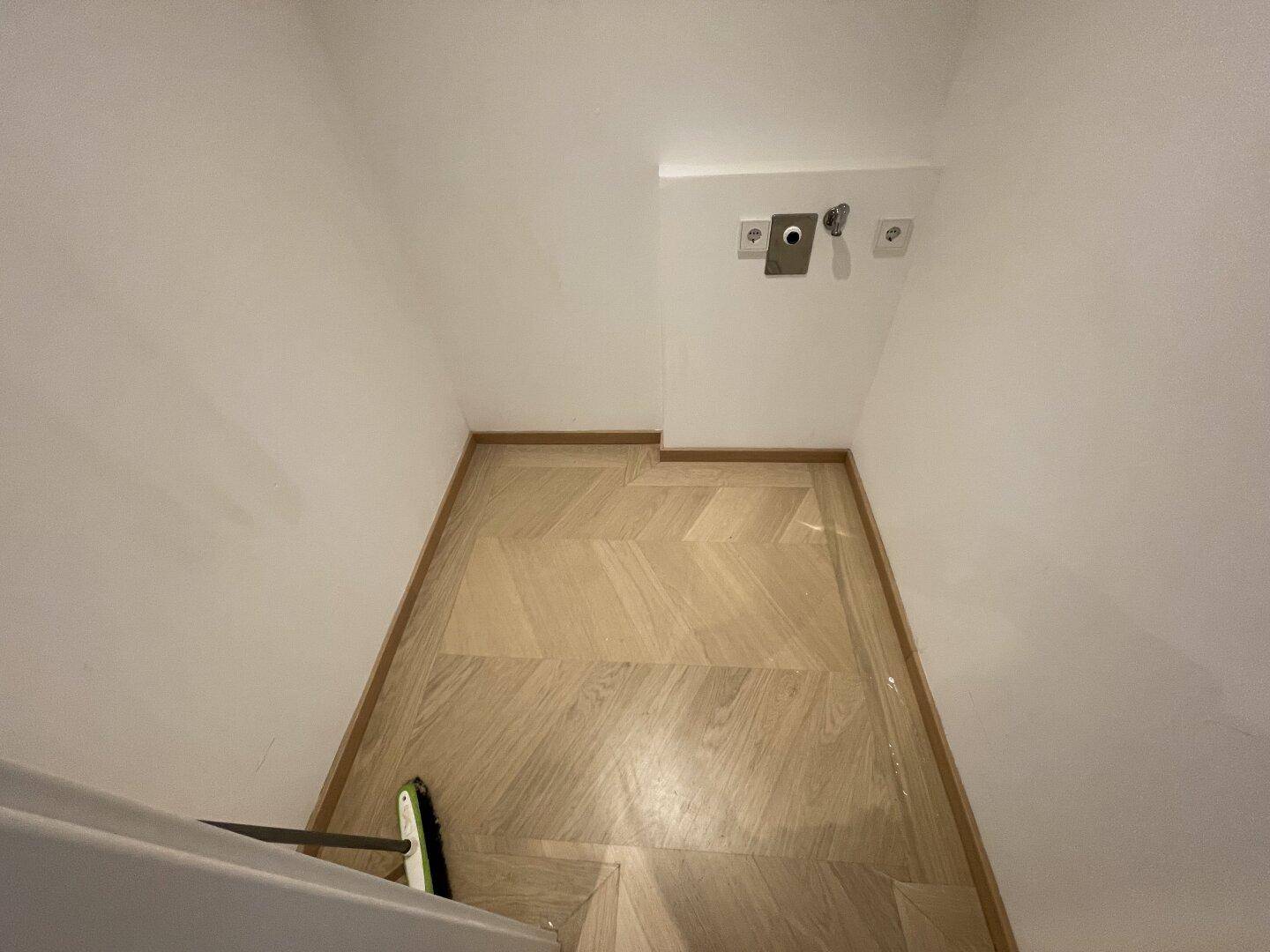 Kleiner Hauswirtschaftsraum mit Fischgrätparkett und Anschlüssen für eine Waschmaschine.