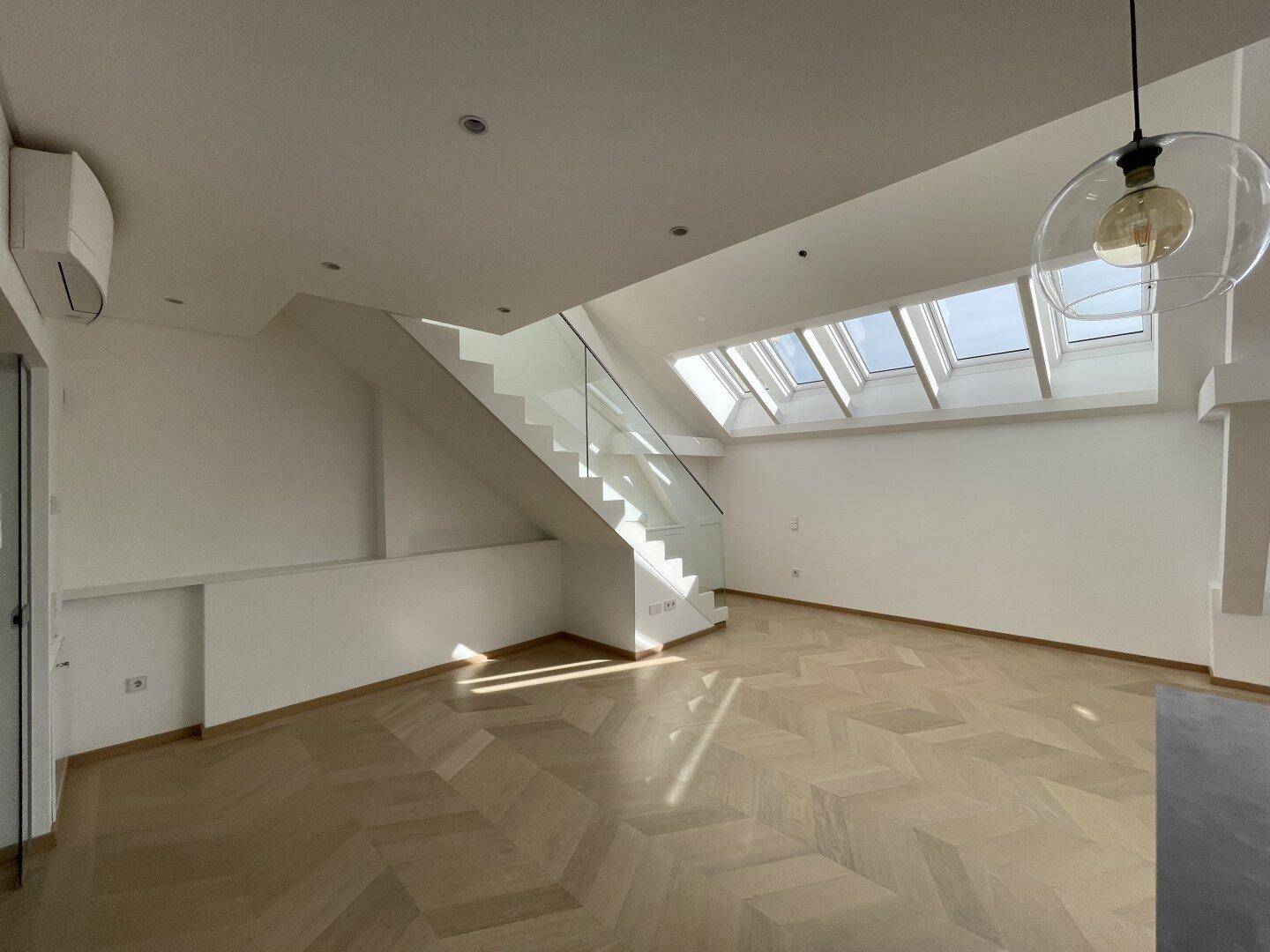 Geräumiger Wohnbereich mit Fischgrätparkett, vielen Dachfenstern und eleganter Glastreppe.