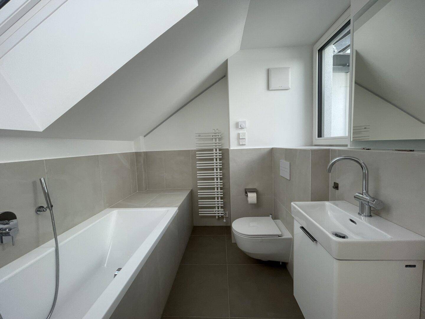 Modernes Badezimmer mit Badewanne, Wand-WC, Einzelwaschbecken und Dachfenster unter Schrägdach.