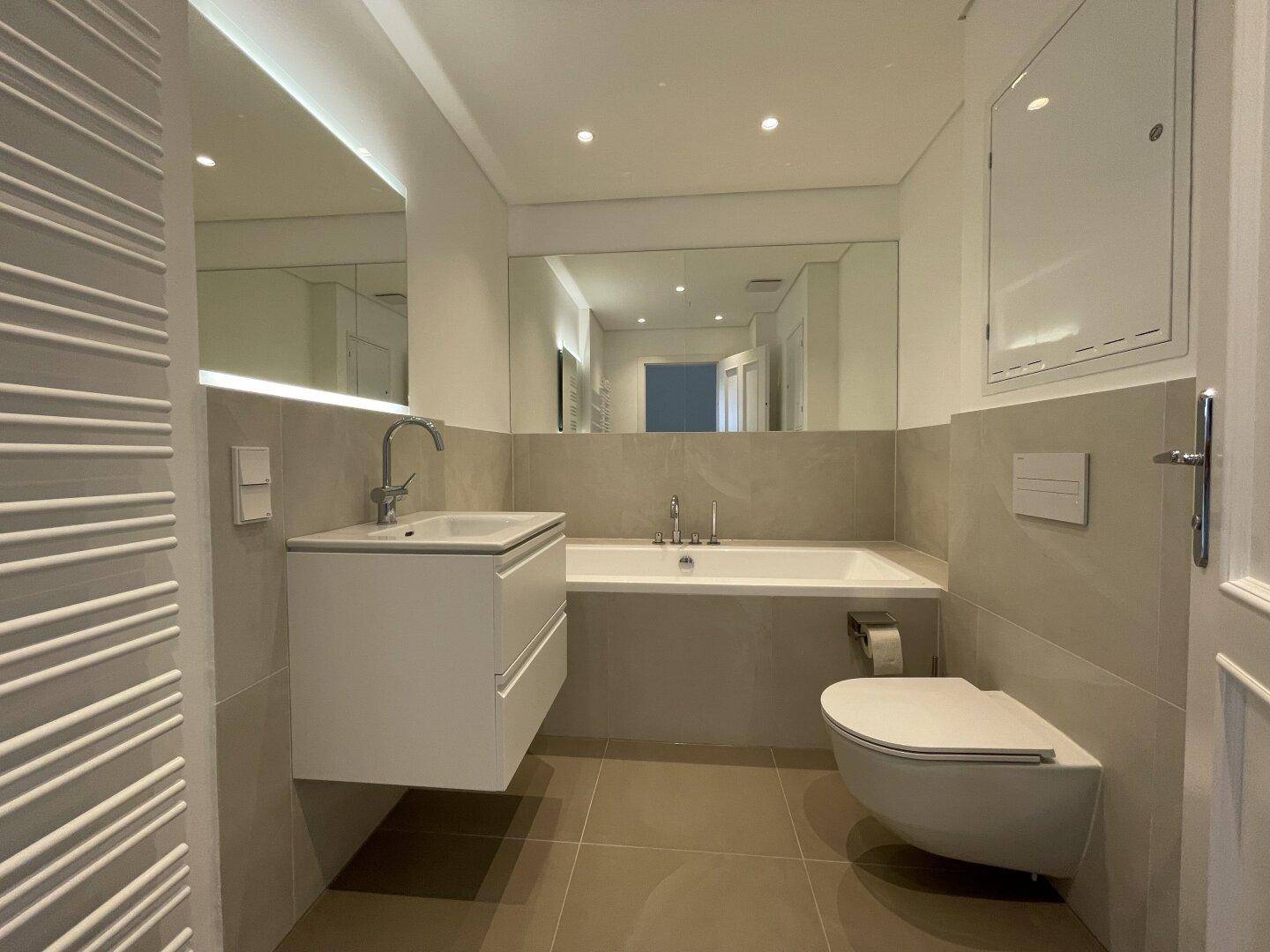 Elegantes Badezimmer mit Badewanne, Wand-WC, Einzelwaschbecken und großem Spiegel.