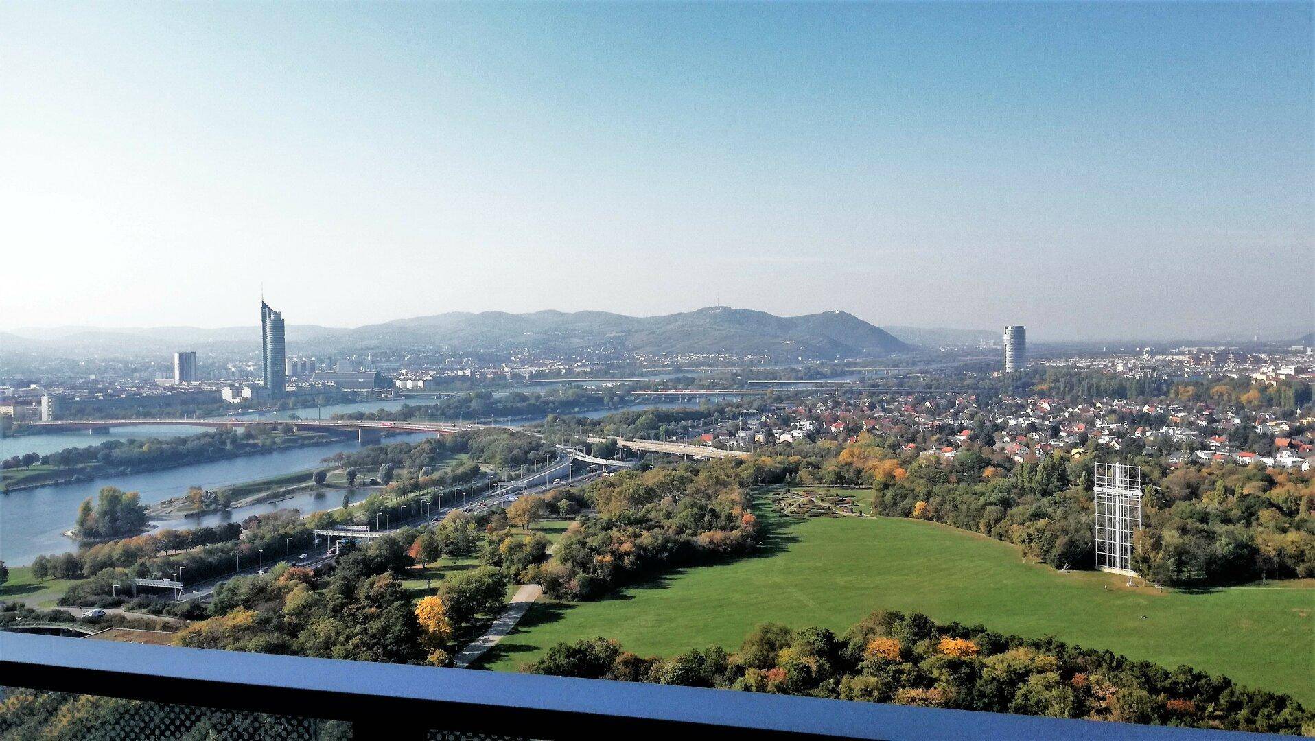 Weitläufiger Panoramablick über Wien mit der Donau, grünen Flächen und städtischer Skyline.