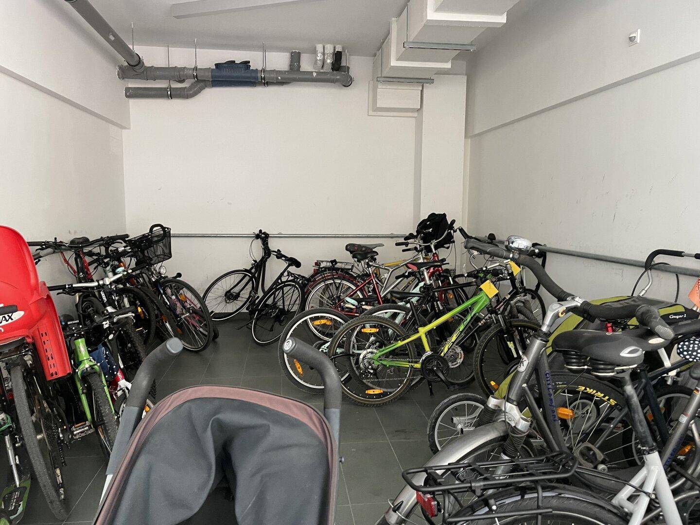 Fahrradraum mit zahlreichen Fahrrädern und Kinderwagen.