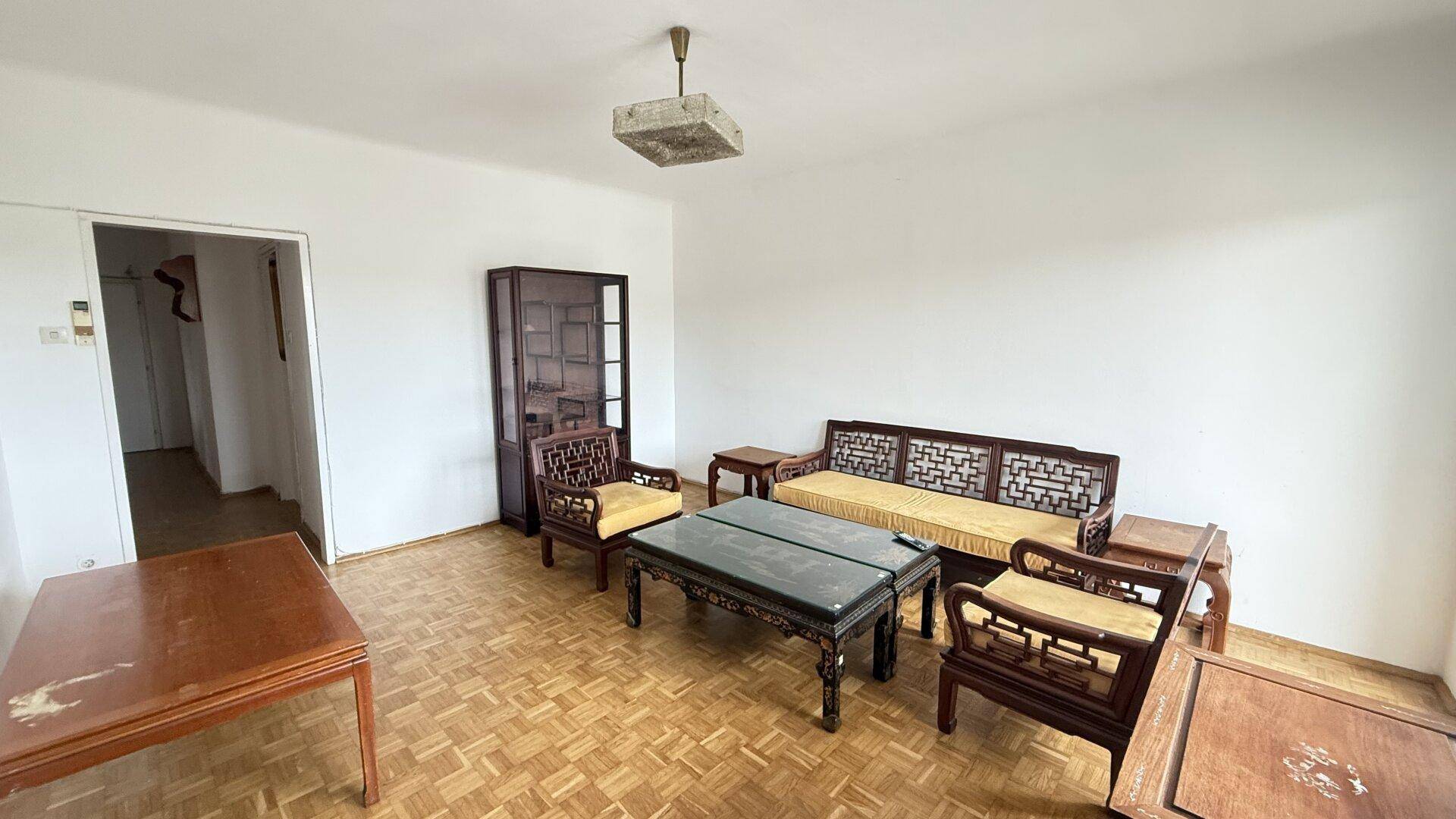 Geräumiges Wohnzimmer mit traditionellen Holzmöbeln und klassischem Parkettboden.