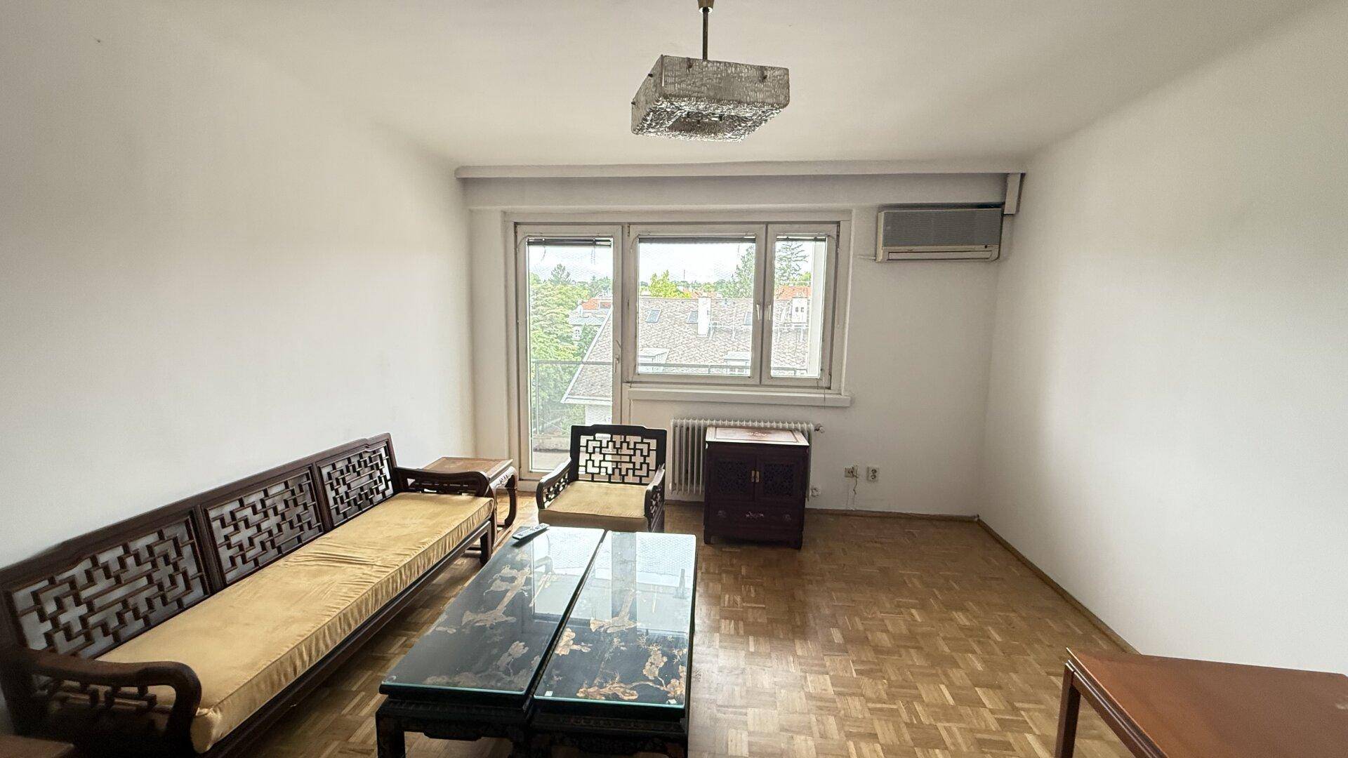 Helles Wohnzimmer mit Parkettboden, Klimaanlage und Blick ins Grüne durch das Fenster.