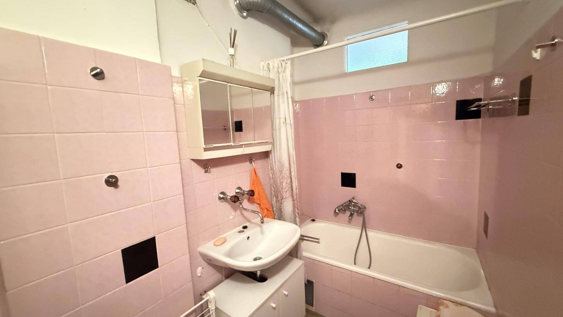 Badezimmer mit rosa Fliesen, Badewanne, Waschbecken und Spiegelschrank im Stil der 80er Jahre.