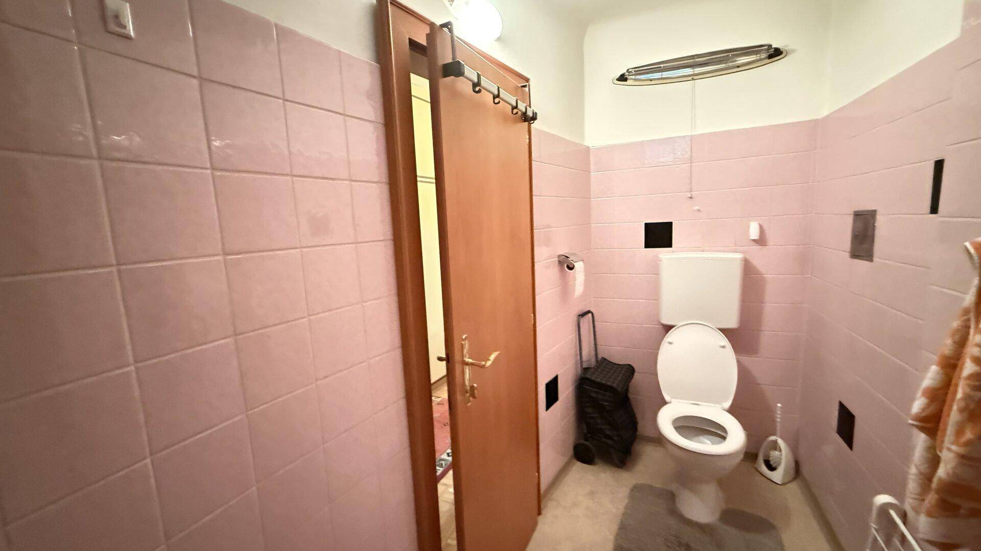 Separates WC mit rosa Fliesen und Toilette.