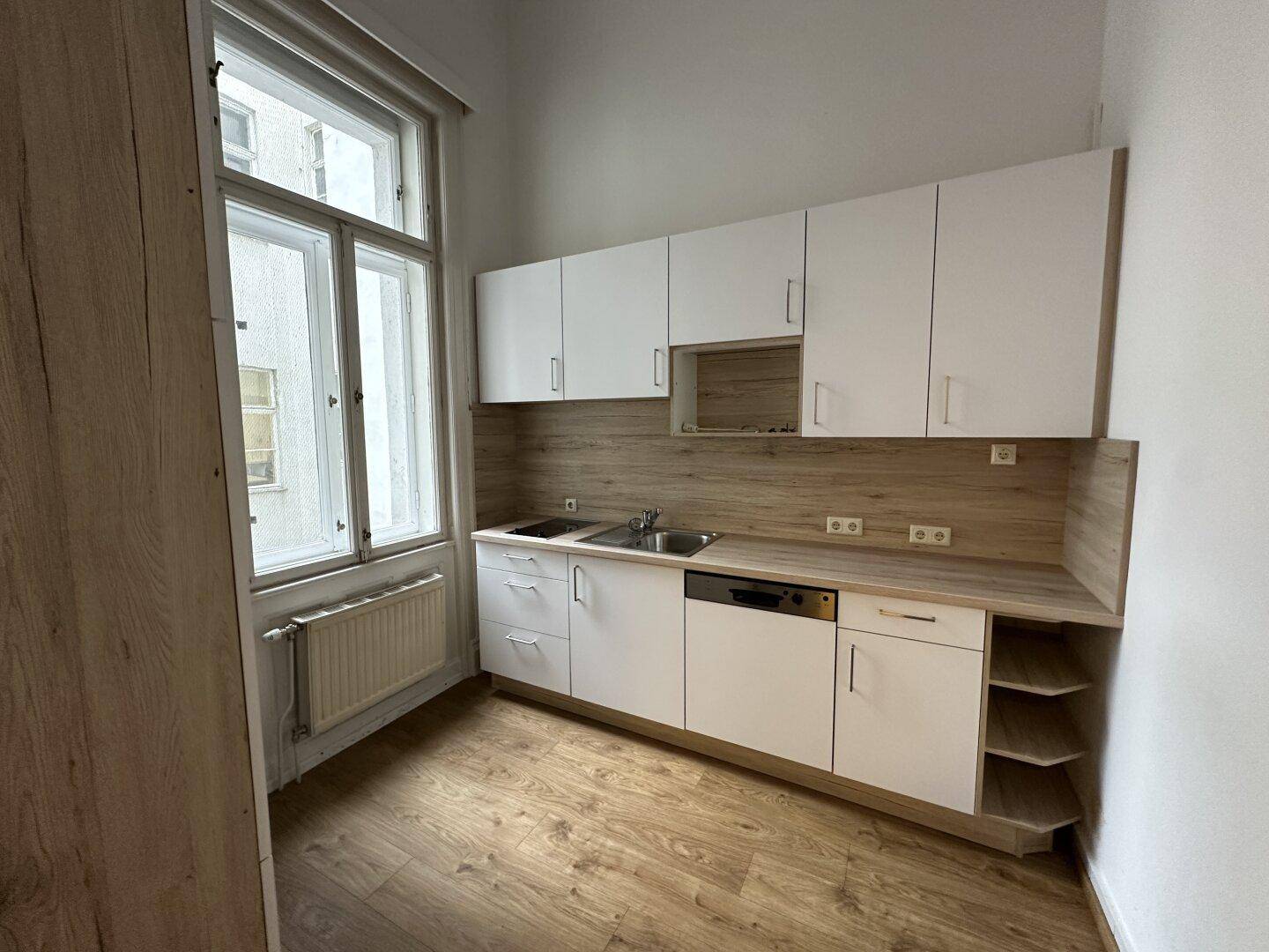 Moderne Einbauküche mit weißen Schränken, Holzoptik-Arbeitsplatte und großem Fenster.