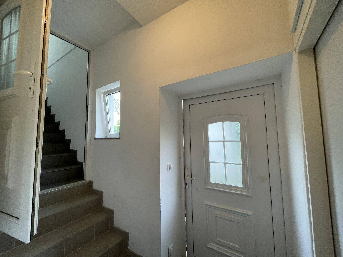 Heller Eingangsbereich mit Treppe zum Obergeschoss und weißer Eingangstür.