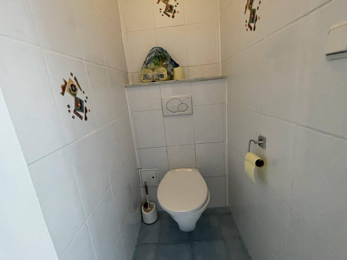 Separates WC mit weißen Fliesen und wandmontierter Toilette, in sauberem Zustand.