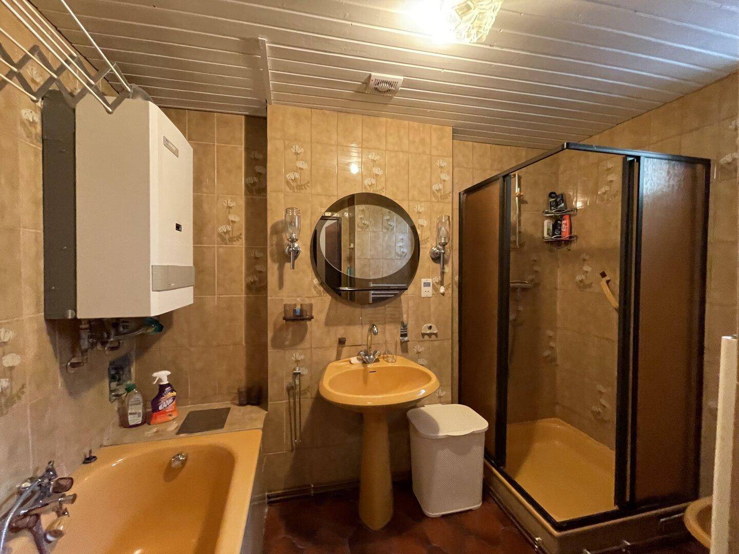 Badezimmer mit Badewanne, Dusche und gelben Fliesen, im Stil der 80er Jahre.