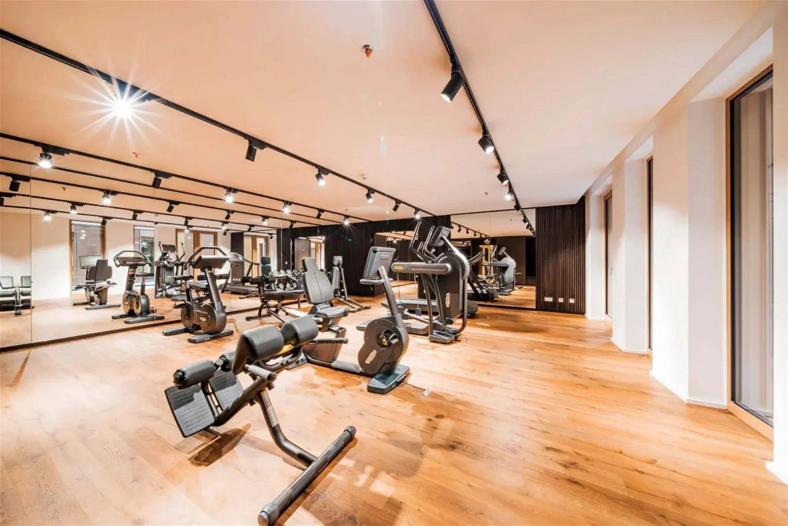 Geräumiger Fitnessraum mit modernen Trainingsgeräten, Holzfußboden und Spiegelflächen.