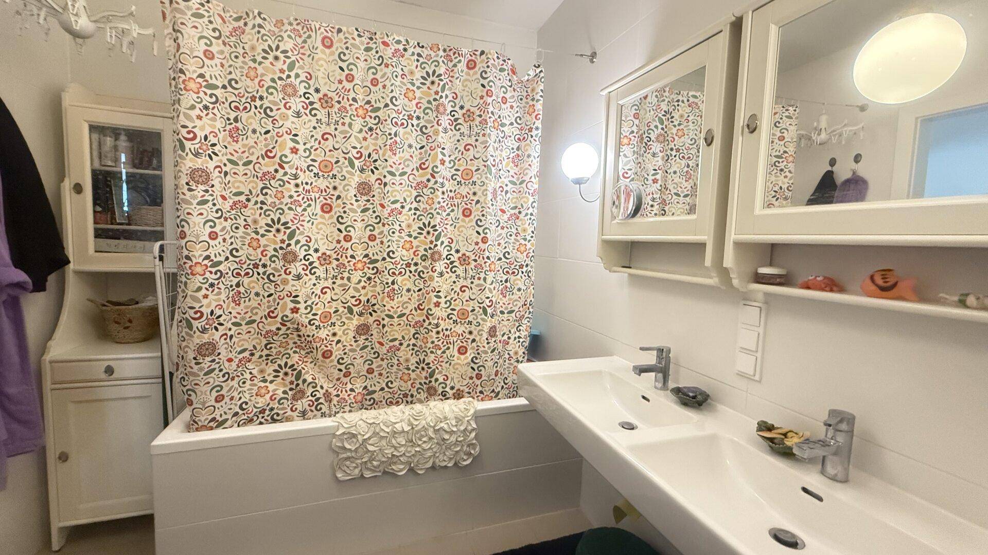 Badezimmer mit Badewanne, Duschvorhang und Doppelwaschbecken.