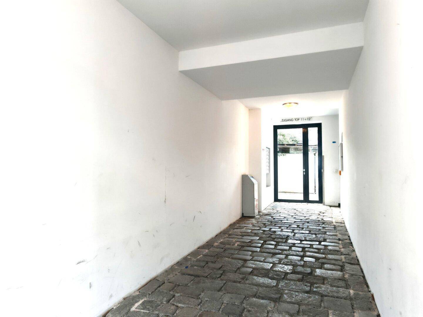 Langer, schmaler Eingangsbereich mit Kopfsteinpflaster und Zugang zum Gebäudeinneren.