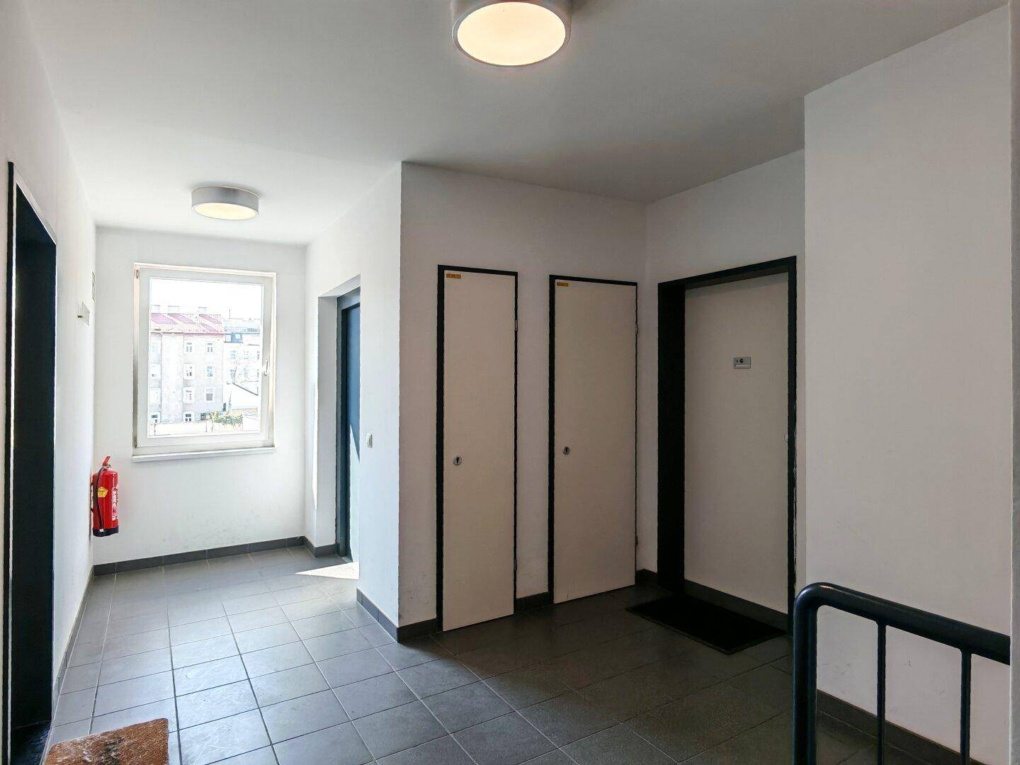 Geräumiger Hausflur mit Fliesenboden, Fenster und Zugang zu mehreren Wohneinheiten.