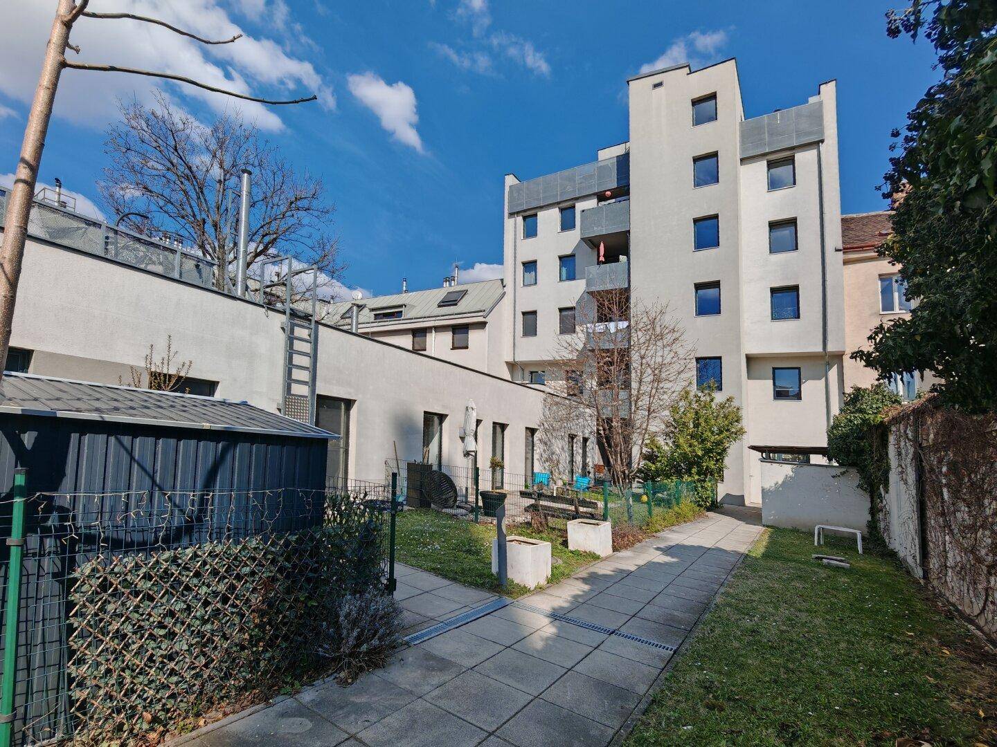 Hinterhofansicht eines Wohngebäudes mit Gemeinschaftsgarten und sonnigen Grünflächen.
