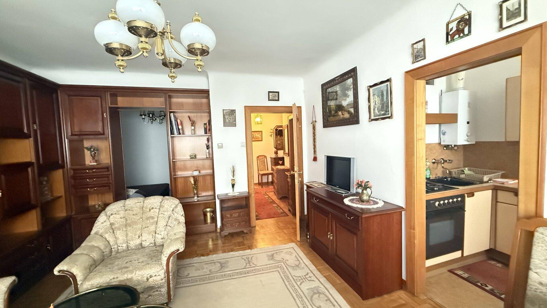 Gemütliches Wohnzimmer mit traditionellen Möbeln und Blick auf eine kleine Küchenzeile.