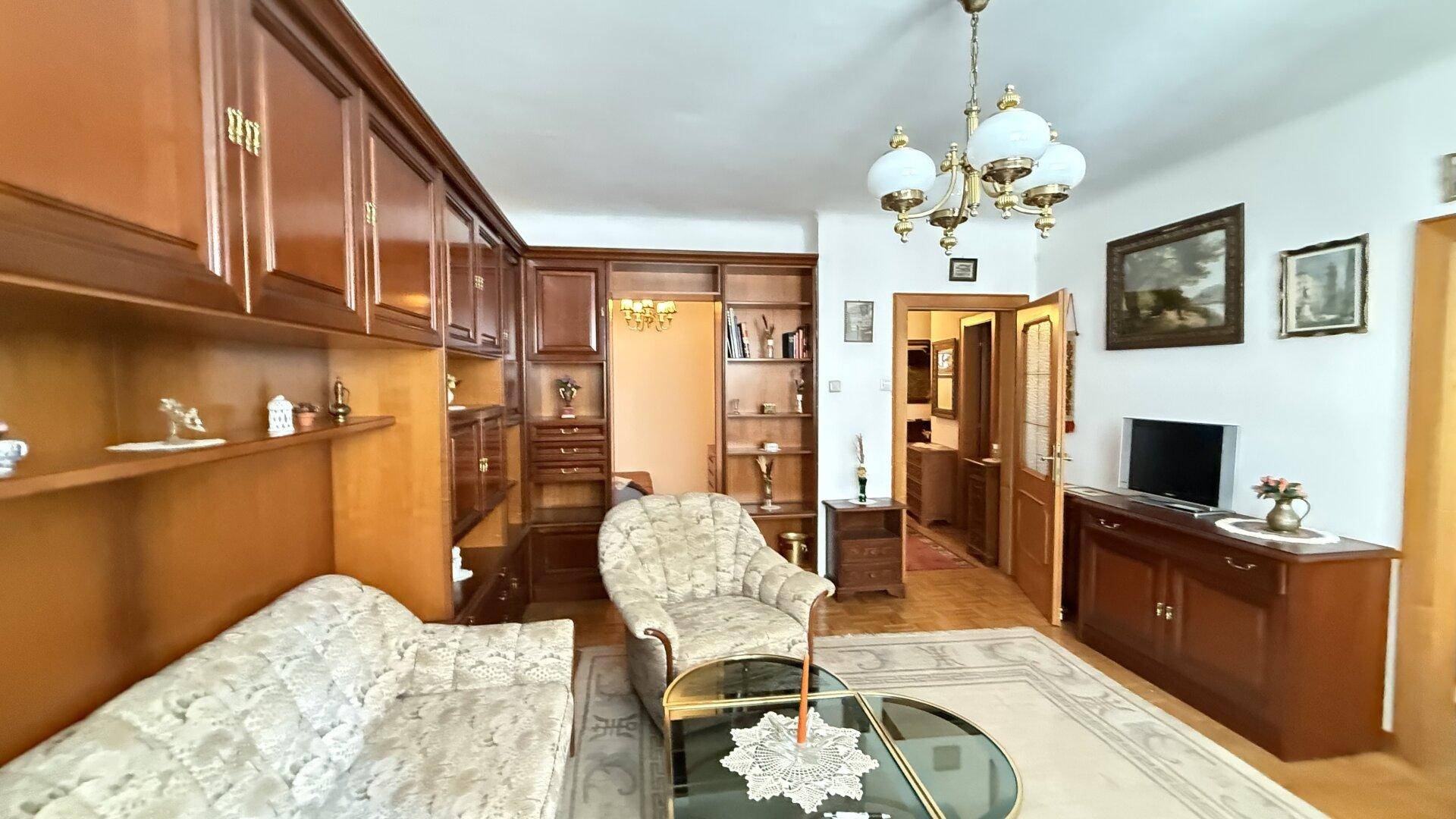 Geräumiges Wohnzimmer mit klassischer Einrichtung, Holzschränken und Kronleuchter.