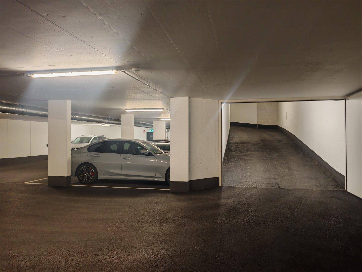 Geräumige Tiefgarage mit mehreren Stellplätzen und einer Rampe zur nächsten Ebene.
