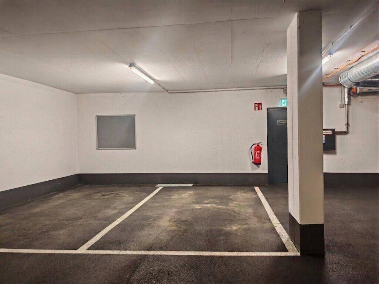 Leerer Stellplatz in einer Tiefgarage mit weiß gestrichenen Wänden und Brandschutzvorrichtungen.